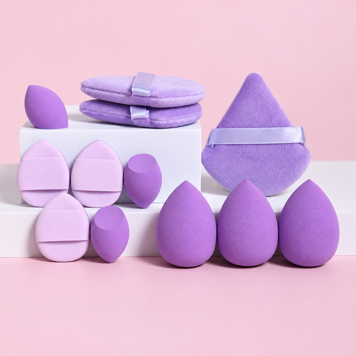 Lila makeupsvampar, mini-svampar och puffar på rosa bakgrund